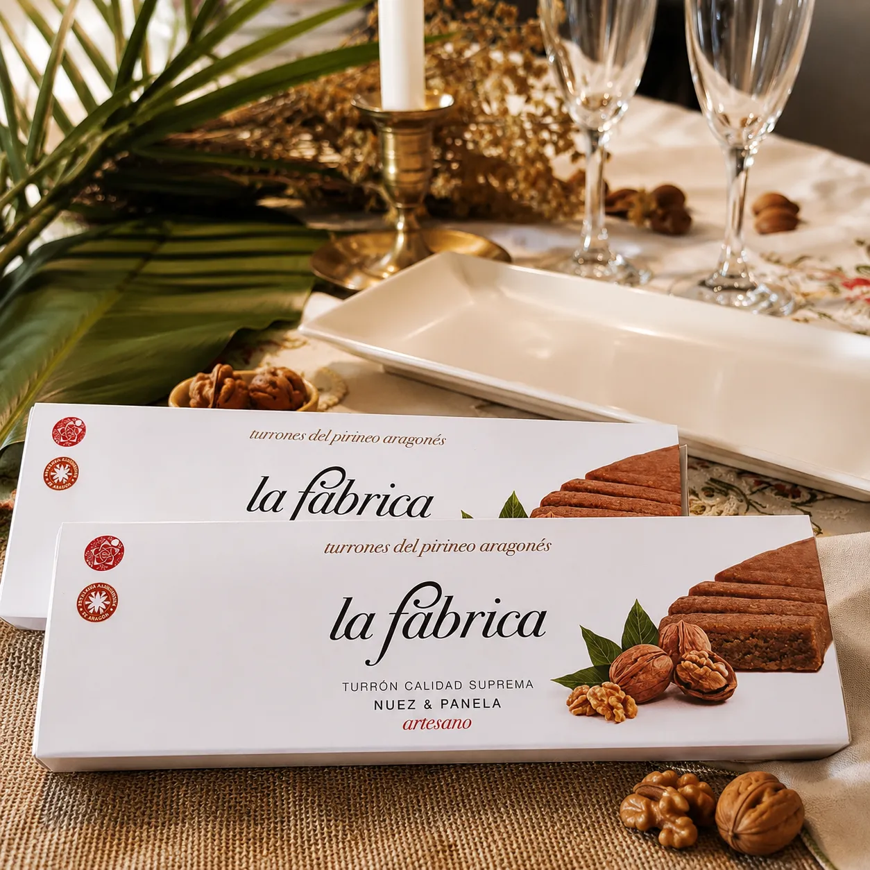 Dos cajas de turrón Nuez & Panela en una mesa con copas y nueces
